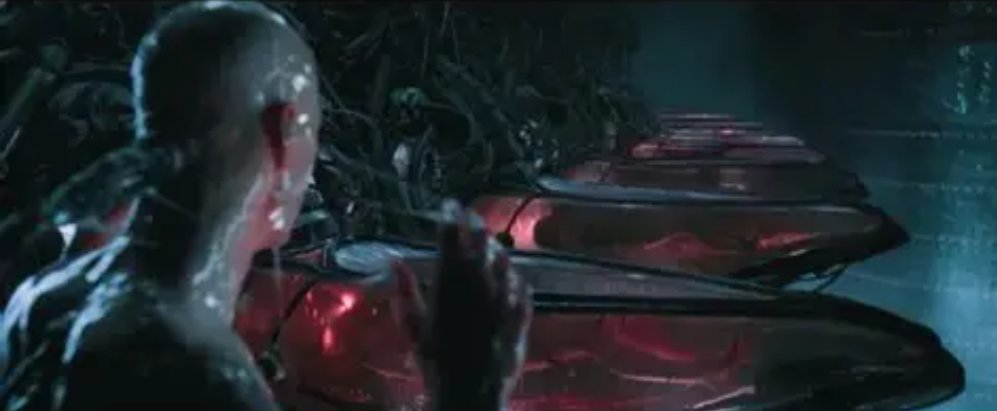 科幻电影画面中,一名剃光头的男子站在红黑色机械舱体前,周围是暗色管线和冷蓝灯光