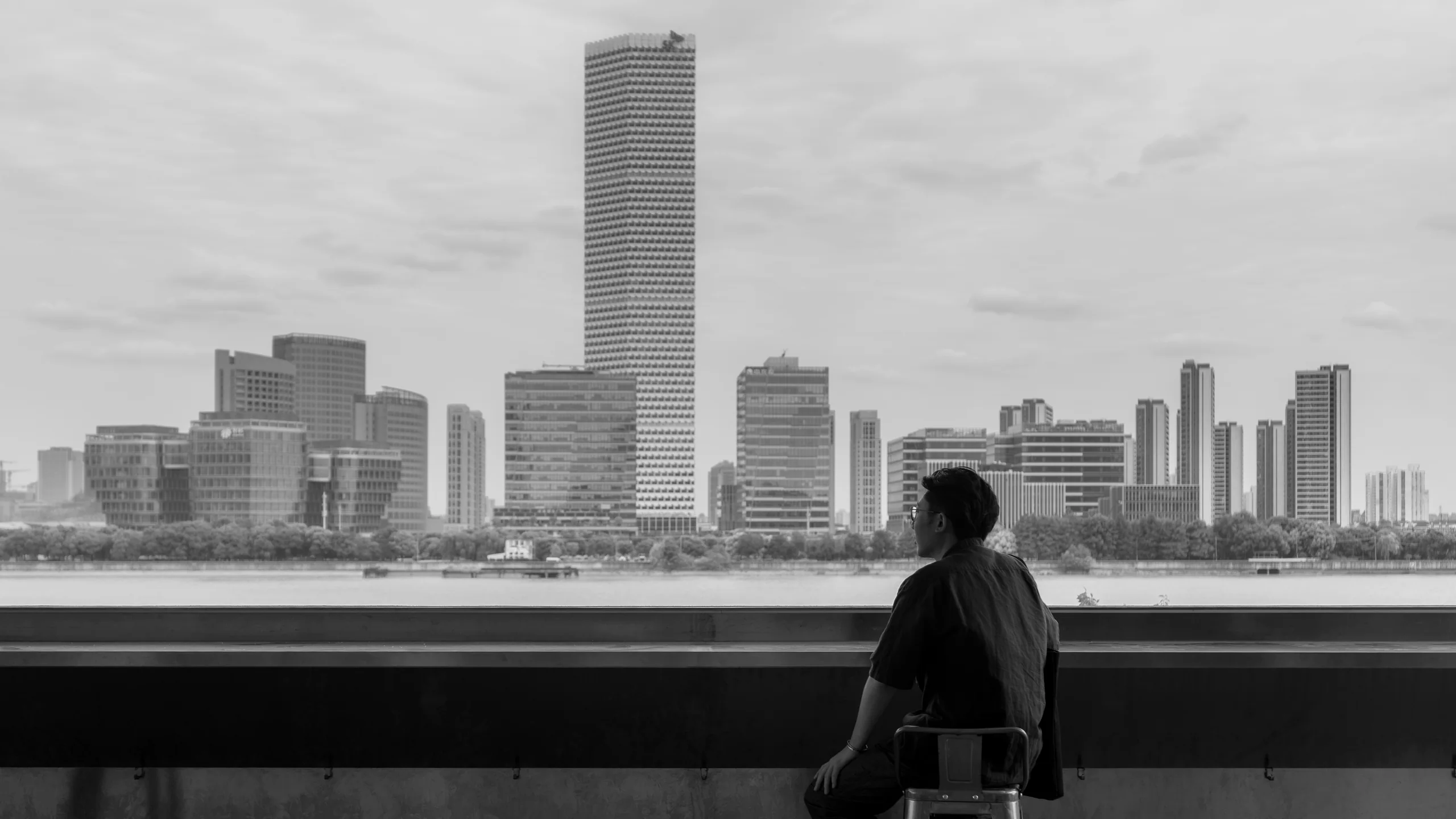 黑白城市景观前，一位人物站在窗边向外眺望